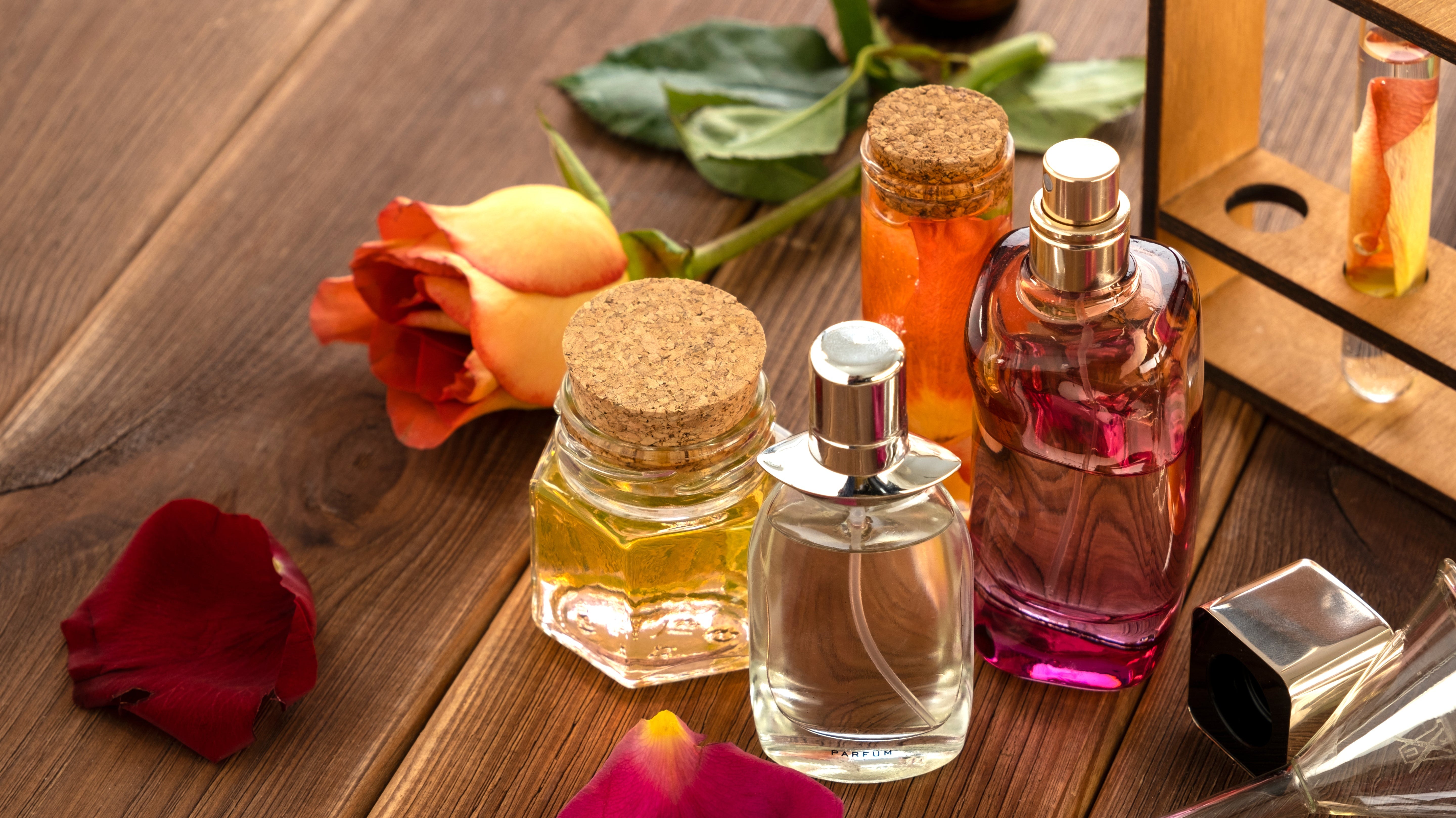 Perfume ingredients in elegant bottles, along with perfume-making glassware and flower petals on a wooden table background.