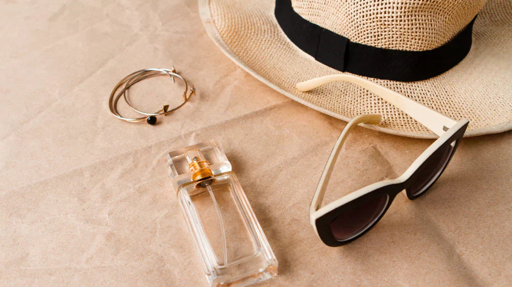 A straw hat, sunglasses, bracelets and a perfume bottle on a plain brown paper background.