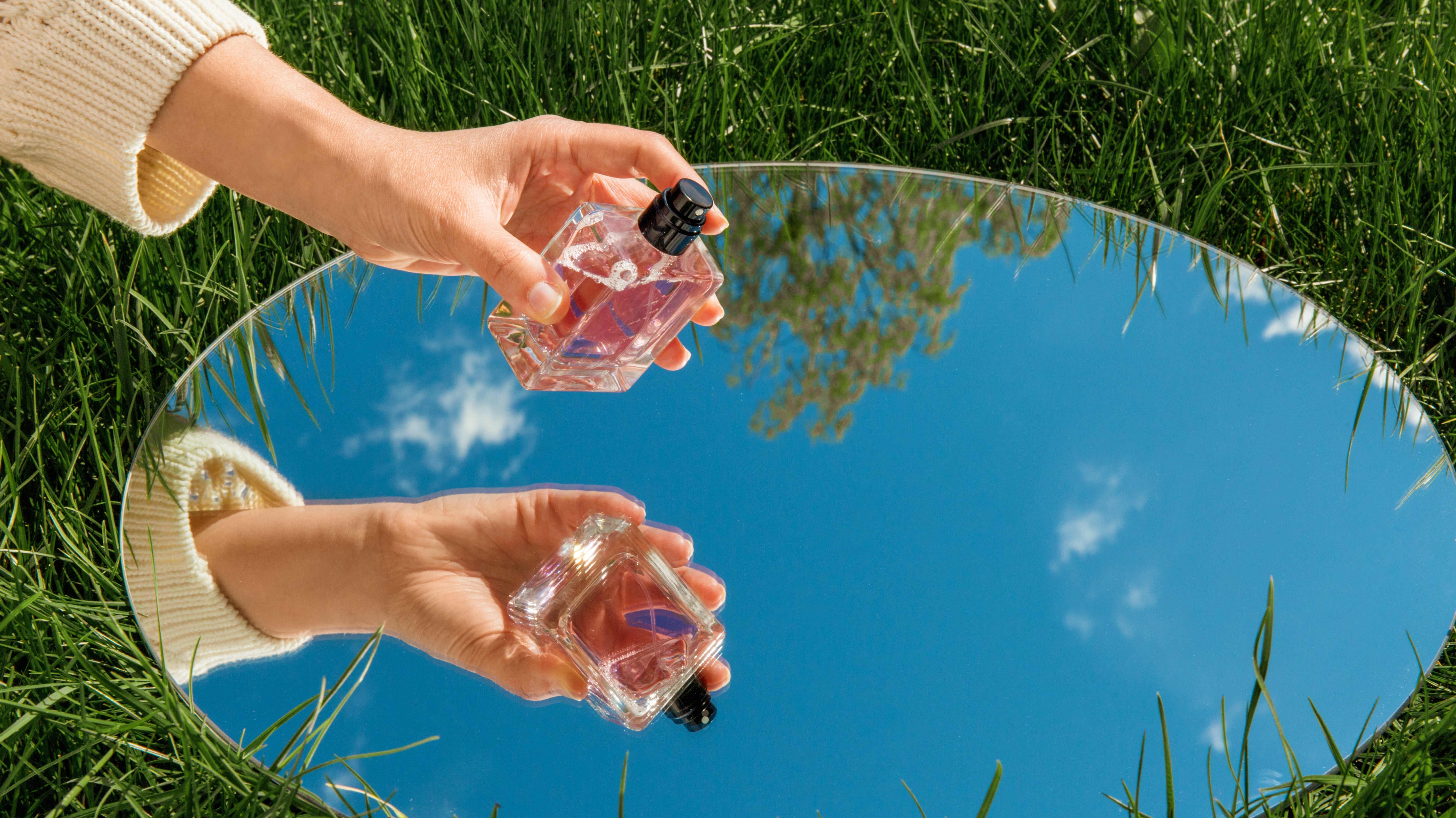 Perfume bottle held in hand, with a mirror reflecting the bottle nad the sky above.