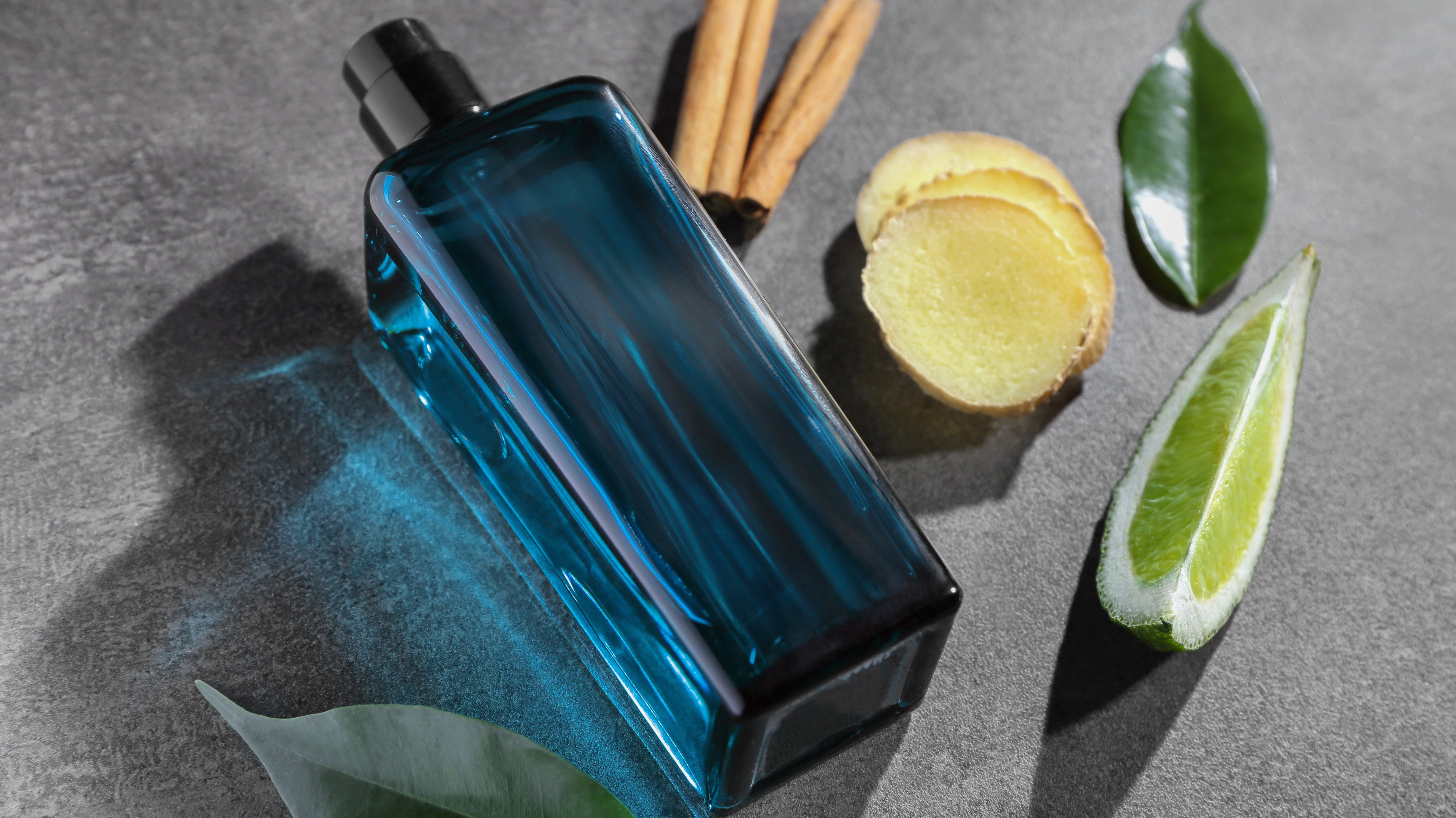 Perfume bottle on a grey background, surrounded by perfume ingredients - lemon, bay leaf, ginger, cinnamon.