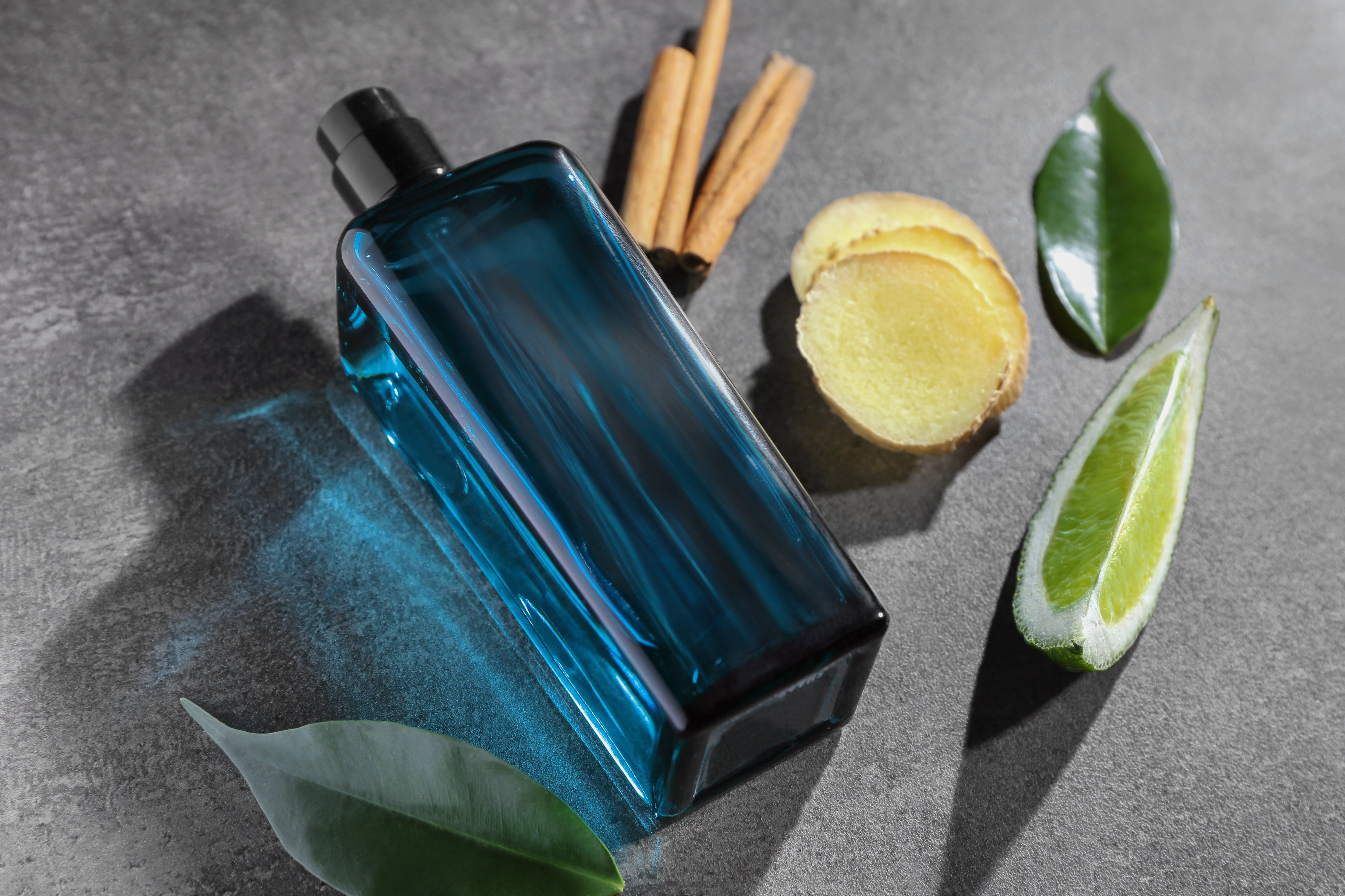 Perfume bottle on a grey background, surrounded by perfume ingredients - lemon, bay leaf, ginger, cinnamon.
