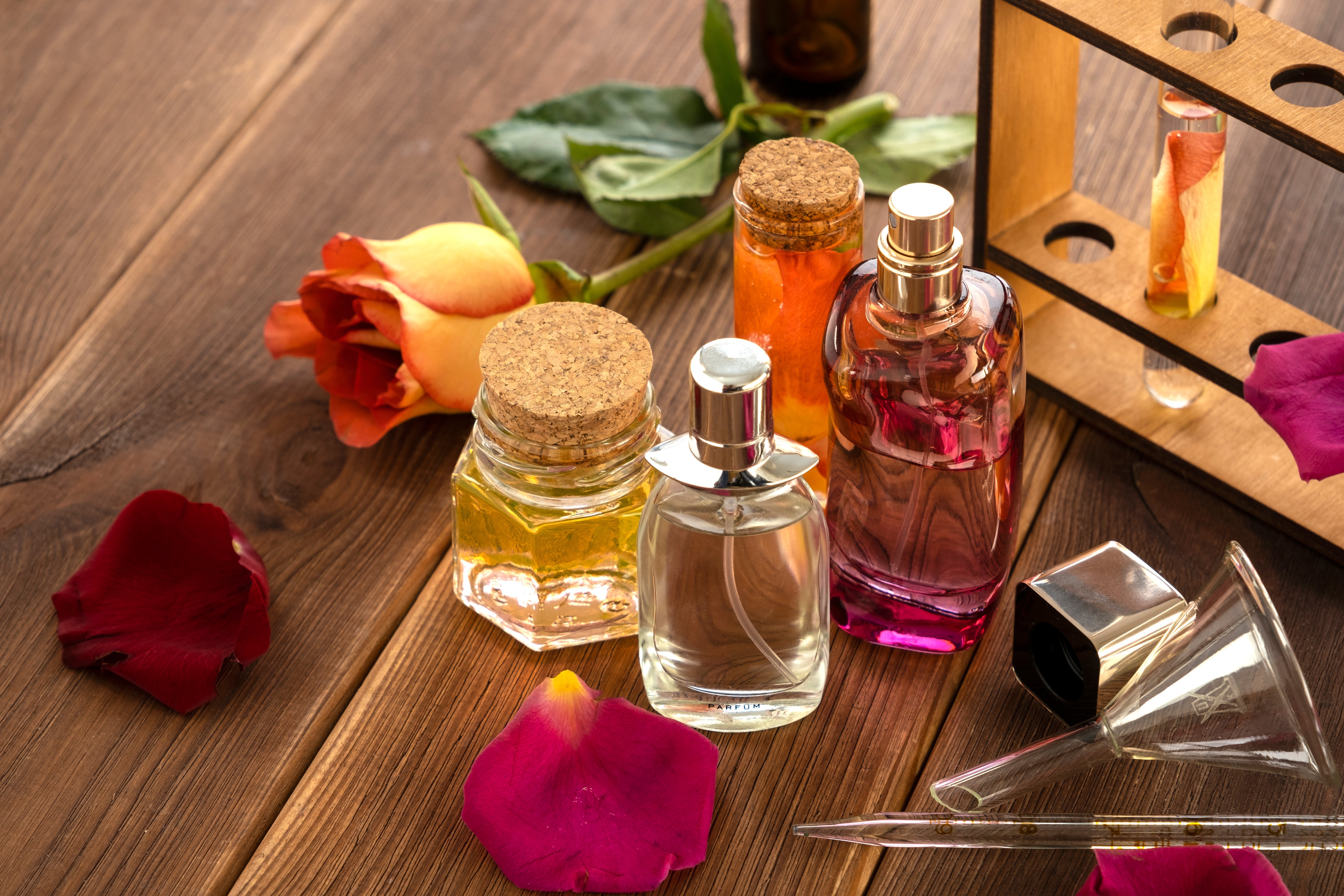 Perfume ingredients in elegant bottles, along with perfume-making glassware and flower petals on a wooden table background.