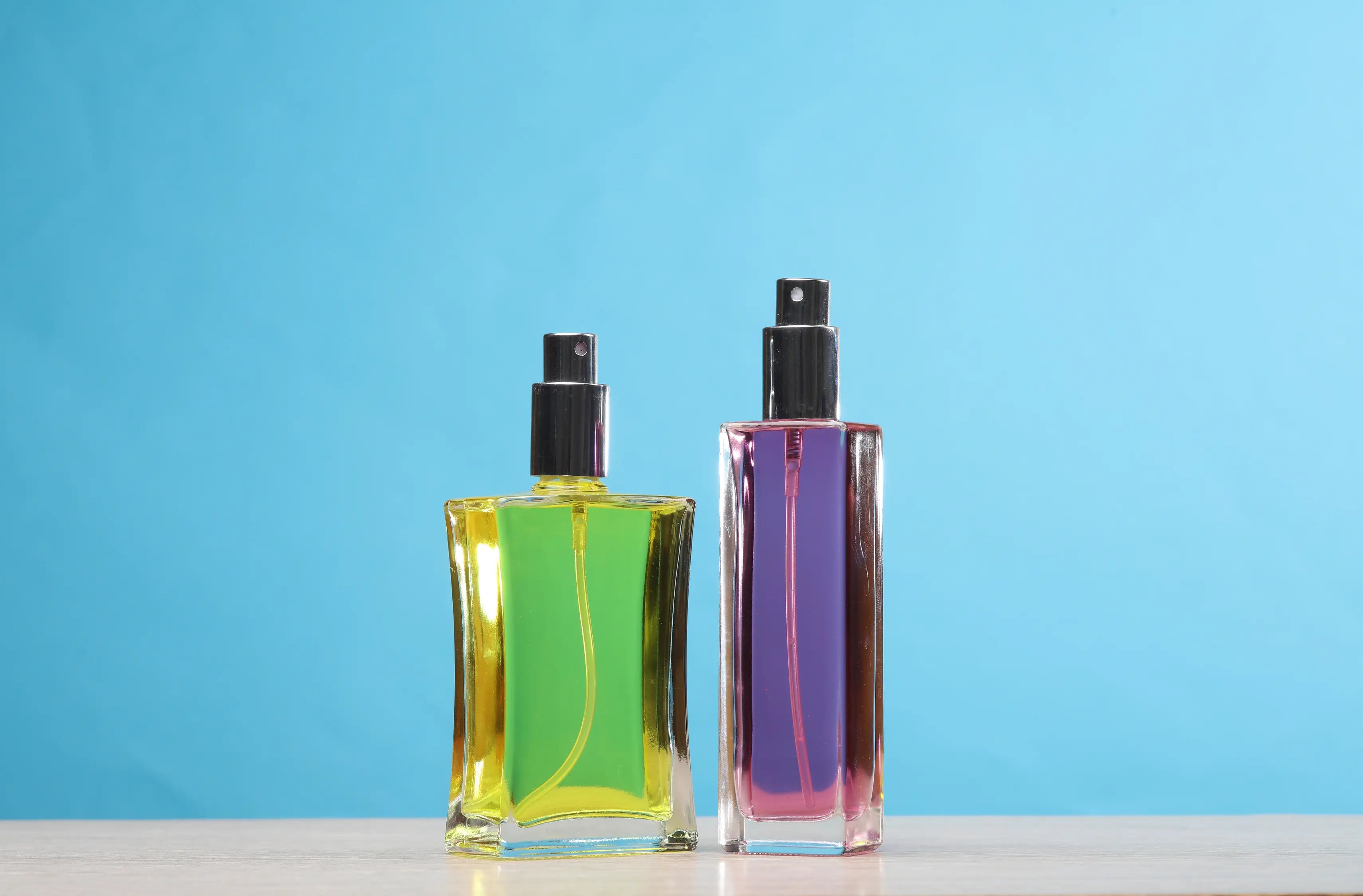 Two perfume bottles in different shapes and colors set on a blue backdrop.