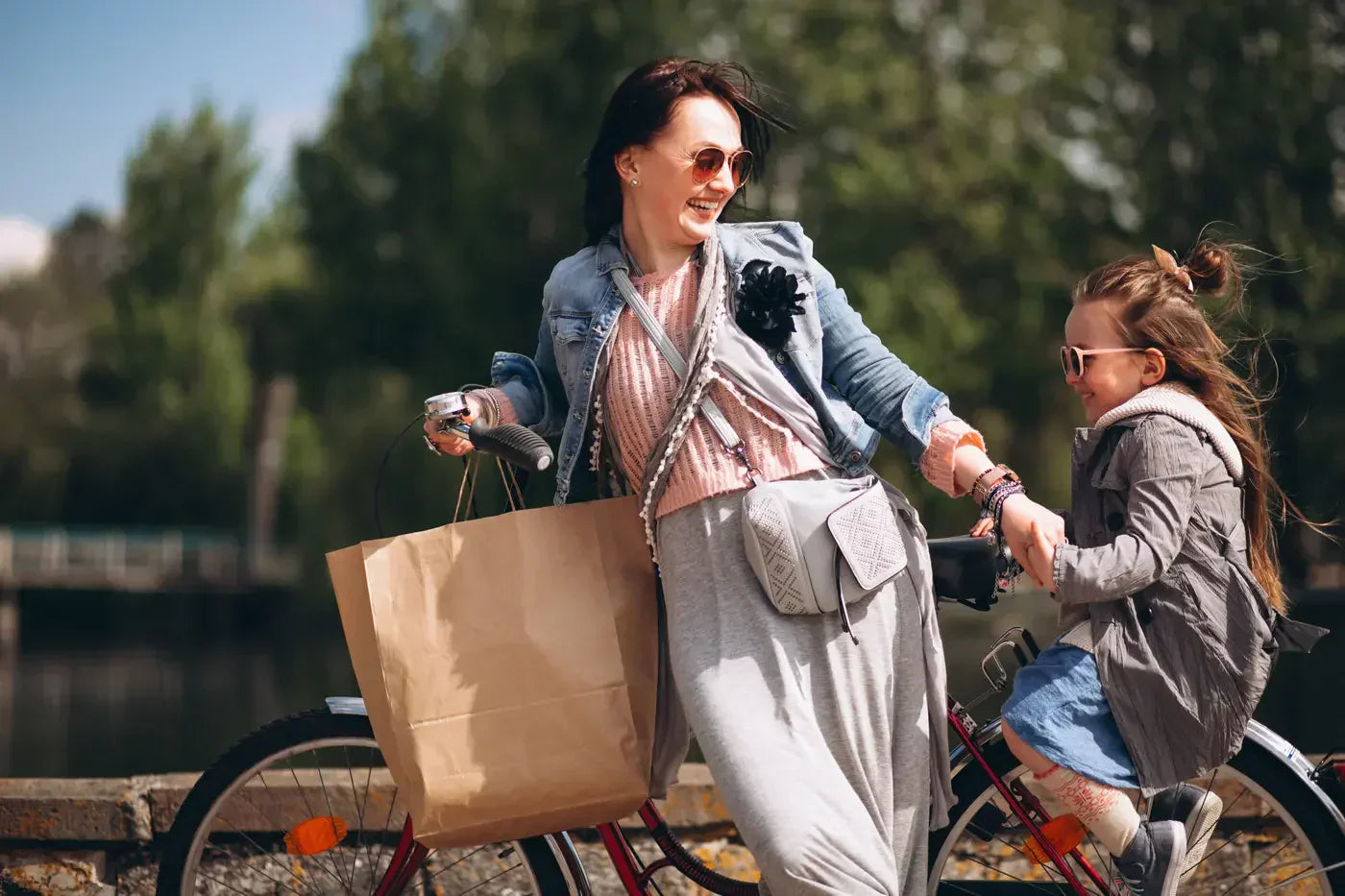 Mother and daughter bicycling on a route near a river. A bridge is faintly visible in the background.