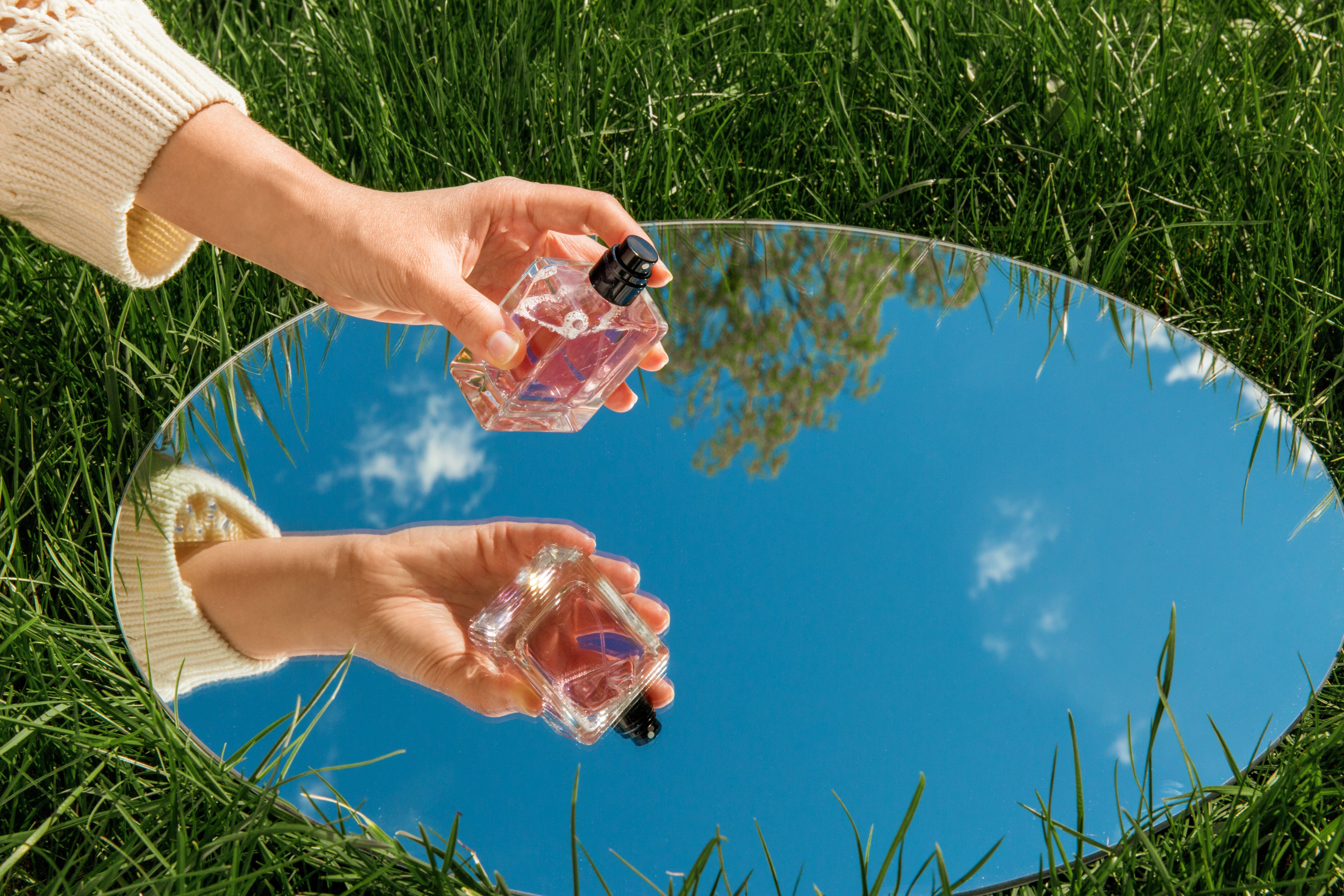 Perfume bottle held in hand, with a mirror reflecting the bottle nad the sky above.